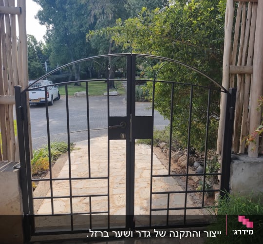 שער מתכת בכניסה עם שביל אבן ועצים ברקע
